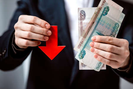 Business person holds roubles and red arrow. Devaluation of the Russian rouble.の写真素材