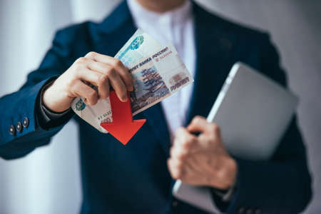 Business person holds roubles and red arrow. Devaluation of the Russian rouble.の写真素材