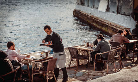 ISTANBUL, TURKEY- october 23, 2014: Waiter serves tea and some snack to a tourist in a street cafe on a coast of Bosphorus in Istanbul, Turkey. Toned image.のeditorial素材