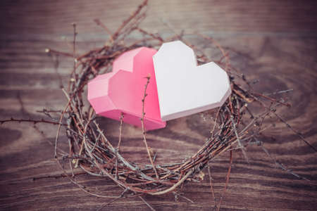 Two pink paper hearts in a small nest on wooden background. Toned picture