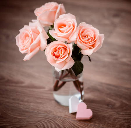 Beautiful pink roses and two valentine\'s paper hearts on wooden background. Toned pictureの写真素材