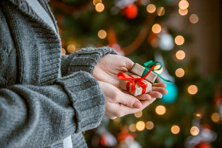 Small gift boxes in woman hands near decorated treeの写真素材
