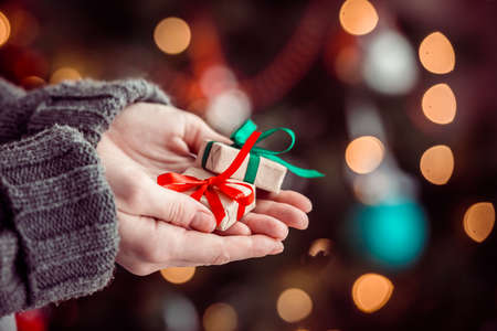 Small gift boxes in woman hands near decorated tree - christmas present, luxury life. Toned pictureの写真素材