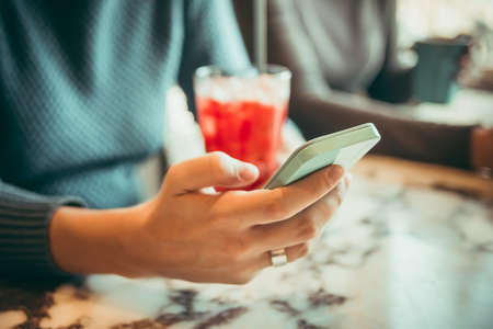 Female hands holding smart phone in cafe. Toned pictureの写真素材