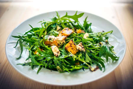 Baked pumpkin, blue cheese and arugula salad on white plateの写真素材