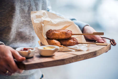 Corndog on a stick with ketchup and mustard on wooden boardの写真素材