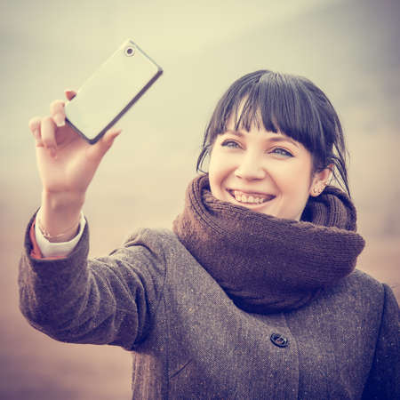 Pretty girl makes selfie with her smart phone. Toned imageの写真素材