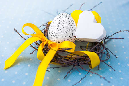 Easter egg and paper heart in a small nest on blue background