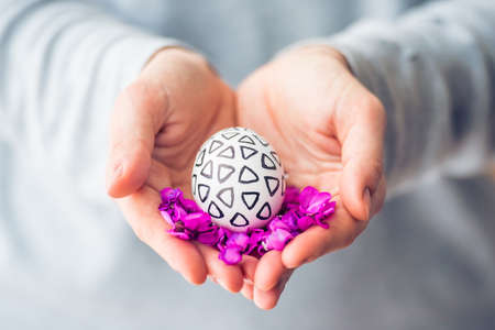 Hands holding modern painted easter egg and violet flowersの写真素材