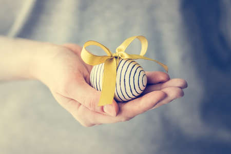Hand holding modern painted easter egg  in ribbon. Toned picture