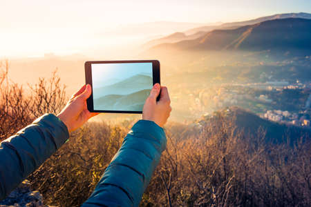 Tourist taking pictures on a tablet in mountains. Toned pictureの写真素材