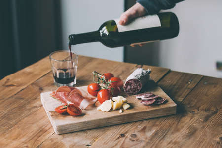 Appetizers - tomato, meat and cheese - on wooden board with bottle of wine and glass. Toned imageの写真素材