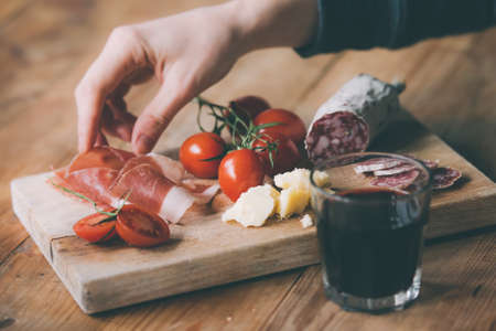 Appetizers - tomato, meat and cheese - on wooden board with  glass of wine. Toned imageの写真素材