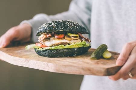 Modern black burger on wooden board in hands. Toned pictureの写真素材