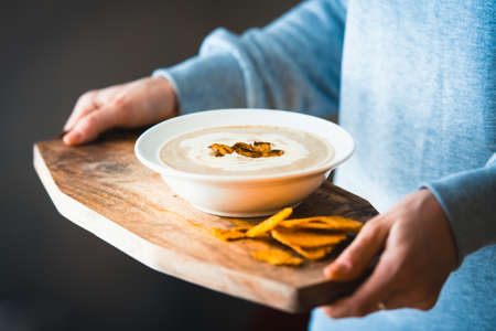 Plate of mushroom cream soup served with  toasts on wooden board in handsの写真素材