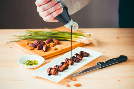 Snack appetizer - dried dates wrapped with bacon and dressed with balsamic creme vinegarの写真素材