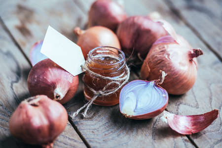 Red onion marmalade in a small glass jar on wooden table. Blank label provides copy space for a messageの写真素材