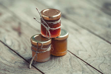 Three small jars of marmalade or jam on wooden table. Toned imageの写真素材