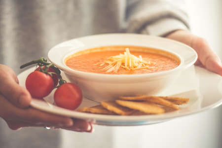 Plate of tomato soup served with cheese and toasts in hands. Toned pictureの写真素材