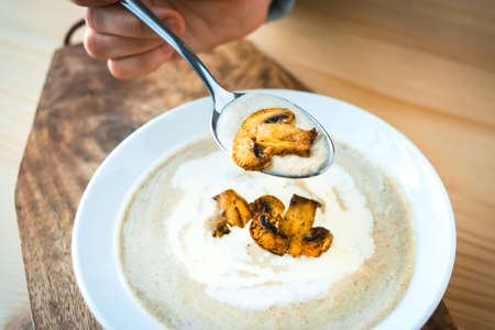 Plate of mushroom cream soup served with  toasts on wooden board and hand with spoonの写真素材