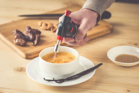 Caramelizing of creme brulee with bourbon vanilla sticks and hand with torch. Toned pictureの写真素材