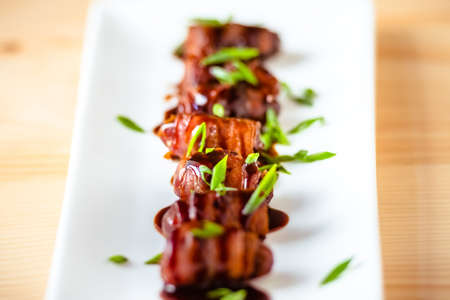 Snack appetizer - dried dates wrapped with bacon and dressed with balsamic creme vinegar and green onions. Selective focusの写真素材