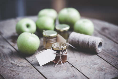 Apple jam in a small glass jar and green apples on wooden table. Blank label provides copy space for a message. Toned imageの写真素材