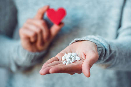 White pills and paper heart in hands. Medicine and health care conceptの写真素材