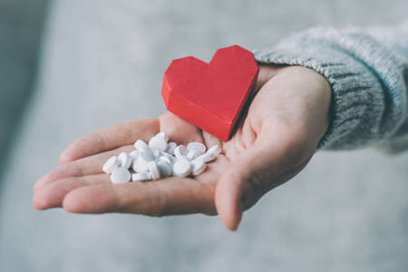 White pills and paper heart in hands. Medicine and health care concept. Toned imageの写真素材