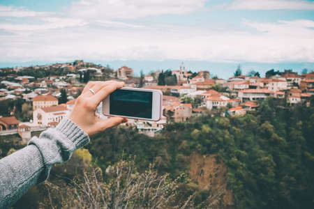 Person with smart phone makes pictures of beautiful old city from the hill. Toned pictureの写真素材