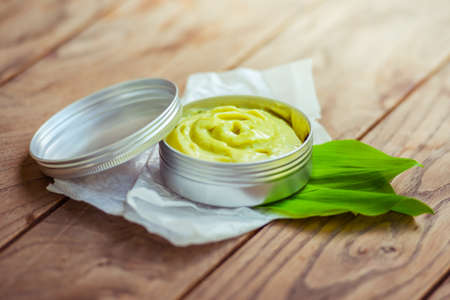 Cosmetic cream container with green herbal leaves on wooden backgroundの写真素材