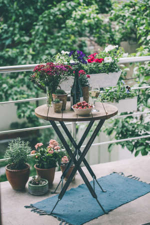 Strawberry, glass of wine and flowers on small wooden table on beautiful terrace or balcony. Toned imageの写真素材