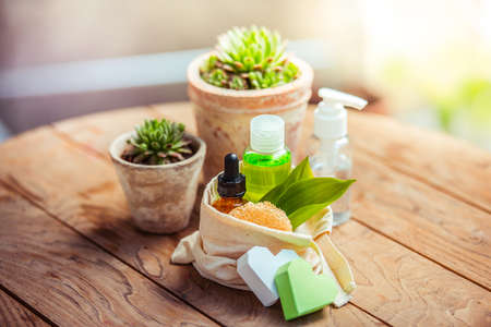 Cosmetic bottle containers with green herbal leaves and garden pots with flowers on wooden backgroundの写真素材
