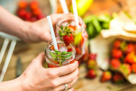 Retro glass jars of lemonade with  strawberries, cucumber and mint in handsの写真素材