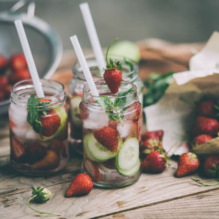 Three retro glass jars of lemonade with  strawberries, cucumber and mint on wooden table. Toned imageの写真素材