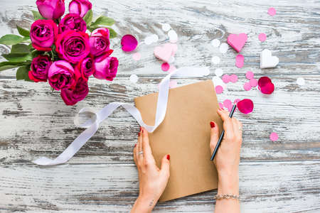 Bouquet of roses and closed book or notebook in female hands on old wooden table. Top viewの写真素材