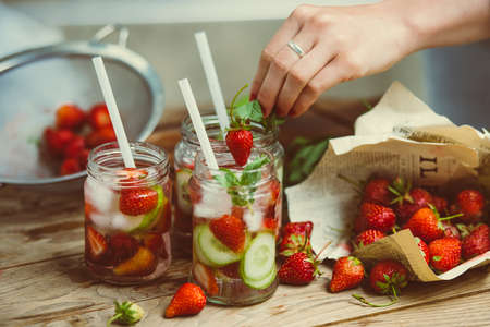 Preparation of lemonade - three retro glass jars, strawberries, cucumber and mint on wooden table. Toned imageの写真素材