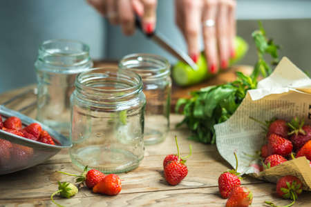 Preparation of lemonade - three retro glass jars, strawberries, cucumber and mint on wooden tableの写真素材
