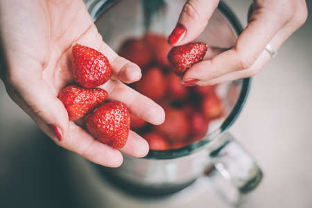 Hands putting fresh strawberries in blender cup. Selective focus. Toned imageの写真素材