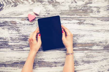 Female hands holding electronic tablet old wooden table. Top view. Toned imageの写真素材