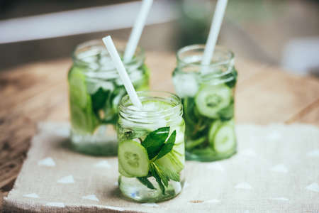 Three retro glass jars of lemonade with cucumber and mint on wooden tableの写真素材