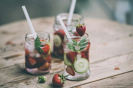 Three retro glass jars of lemonade with  strawberries, cucumber and mint on wooden table. Toned imageの写真素材