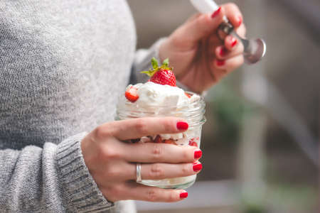 Hands holding classic british summer dessert called Eton Mess. Strawberries, crushed meringue and whipped cream in jarの写真素材