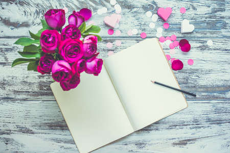 Bouquet of roses and open notebook on old wooden table. Top view. Toned imageの写真素材