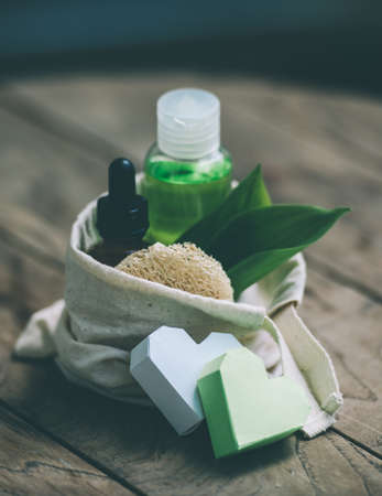 Cosmetic bottle container with green herbal leaves in small organic cotton bag on wooden background. Toned imageの写真素材