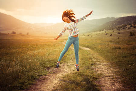 Beautiful girl jumping on the rural roadの写真素材