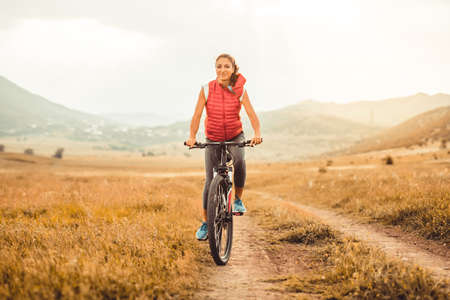 Beautiful girl riding on bicycle outdoor on the rural roadの写真素材