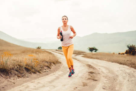 Beautiful girl running on a rural road during sunsetの写真素材