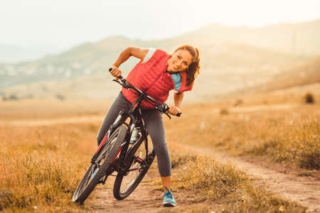 Beautiful girl riding on bicycle outdoor on the rural roadの写真素材