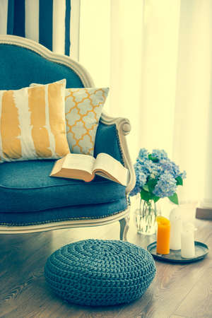 Cozy armchair with open book and decorative pillows. Interior and home decor concept. Toned imageの写真素材